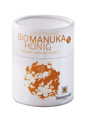Ein Glas SONNENTOR HONIG MANUKA mit der Aufschrift „Bio Manuka Honig“ und „Sonnentor“ zeigt eine Abbildung von Blumen und Bienen.