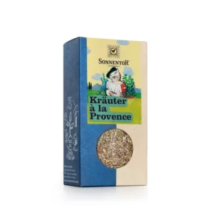 Eine Schachtel SONNENTOR KRÄUTER A LA PROVENCE, eine dekorative Verpackung mit einem transparenten Fenster, durch das die getrockneten Kräuter im Inneren sichtbar sind.