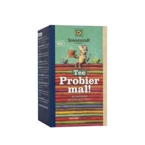 Der SONNENTOR TEE PROBIER MAL zeigt eine Schachtel mit einer Katze, die eine Teetasse hält, dahinter sind bunte Teeschachteln gestapelt. Er trägt den Text „Tee Probier mal!“ und bietet 20 Sorten Bio-Tee.