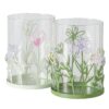 Das DEKO WINDLICHT BLOSSOM Set besteht aus zwei klaren zylindrischen Behältern mit pastellgrünen und violetten Blumenmustern, grünen Böden und ausgeschnittenen Blumen und Blattmustern um die Böden.