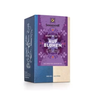 Eine Schachtel SONNENTOR TEE HAPPINESS IS AUF BLÜHEN Kräutertee mit Rose, Sonnenhut und Schlüsselblume. Die lila-beige Verpackung ist mit floralen Motiven verziert.