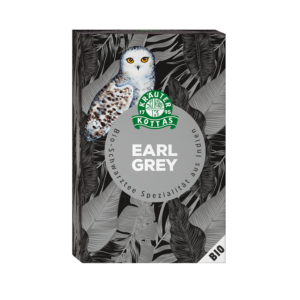 Auf der Schachtel von KOTTAS TEE EARL GREY sind eine weiße Eule, ein botanischer Hintergrund und ein deutscher Text abgebildet, der darauf hinweist, dass es sich um Bio-Schwarztee aus Indien handelt.
