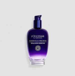 Eine violett-blaue Pumpflasche IMMORTELLE PRECIEUSE EMULSION von LOccitane en Provence steht vor einem hellgrauen Hintergrund.