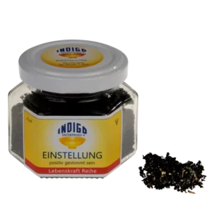 In einem Glas mit der Aufschrift „Indigo Enterprises EINSTELLUNG – positiv gestimmt sein“ und einem kleinen Haufen Inhalt daneben befindet sich eine dunkle Kräuter- oder Teemischung.