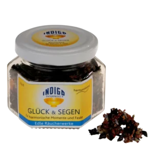 Glas GLÜCK & SEGEN-Räucherstäbchen von Indigo Enterprises mit Räucherstäbchen daneben. Auf dem gelben Etikett steht „für harmonische Momente und Feste“.
