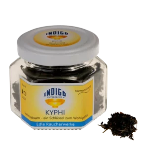 Glasgefäß mit der Aufschrift „KYPHI – Seelenbalsam, ein Schlüssel zum Wohlgefühl“, das eine dunkle, getrocknete Substanz enthält, von der eine kleine Menge außen sichtbar ist.