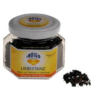 Ein sechseckiges Gefäß mit der Aufschrift IND RW INSPIRATION, das dunkle getrocknete Blätter enthält und neben einem kleinen Stapel derselben Blätter steht.