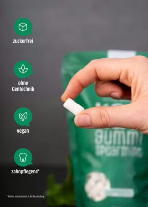 Eine Hand hält ein weißes Stück Kaugummi vor einer grünen Packung XUCKER XYLIT KAUGUMMI 10170, die zuckerfrei, gentechnikfrei, vegan und zahnfreundlich ist.