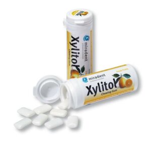 Abgebildet sind zwei Behälter von MIRADENT XYLIT.GUM FR. Einer ist geöffnet und es fallen weiße Gummistücke heraus.