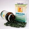 Eine schräge Flasche mit HAFESAN SPIRULINA 400MG KPS-Kapseln neben ihrer Verpackung.