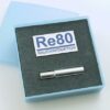 Eine metallische Zigarettenspitze in einer blauen Schachtel mit der Aufschrift „RE80 Raucherentw.+Red.Hilfe“.