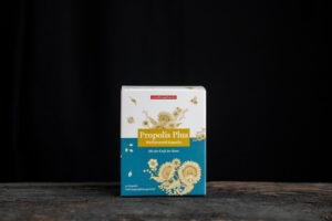 Schachtel mit „PROPOLIS KPS PLUS OEKOPAN“-Kapseln mit Bildern von Blumen und Bienen auf dunklem Hintergrund.