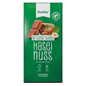 Eine Packung XUCK XYL SCHOKO NUSS 10083 zeigt ein grünes Design mit der Aufschrift Haselnuss ohne Zuckerzusatz und Abbildungen von Milchschokoladenstücken und Haselnüssen.